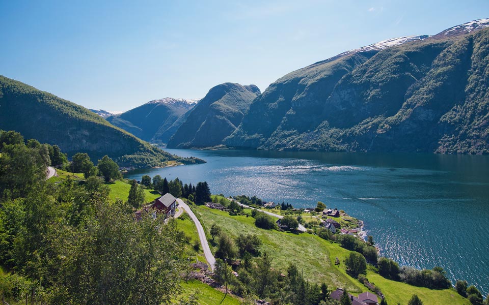 Scenic view of a fjord surrounded by lush green hills and mountains under a clear blue sky | MSC Cruises