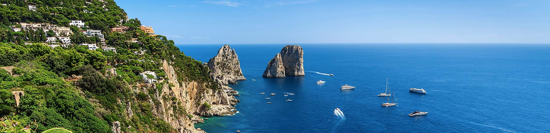 The Faraglioni rock formations off the coast of Capri with yachts in a vibrant blue sea | MSC Cruises The Faraglioni rock formations off the coast of Capri with yachts in a vibrant blue sea | MSC Cruises