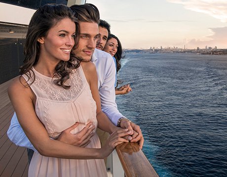 Couple enjoying ocean views from a cruise ship balcony with a city skyline in the distance | MSC Cruises
